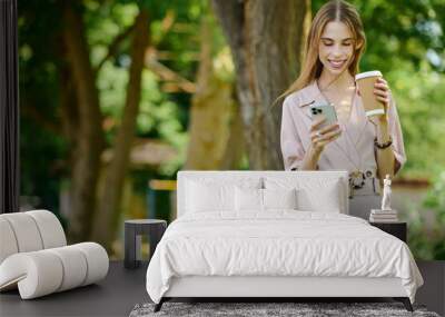 A cheerful young woman with anorexia embraces her outdoor surroundings, sipping coffee and connecting with friends on her phone, radiating happiness. Wall mural