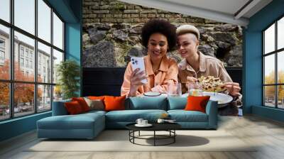 A diverse couple of women enjoying a meal together at a table in a cafe. Wall mural