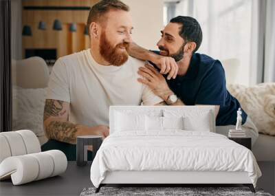 A gay couple in casual attire relax on a couch, enjoying each others company and sipping coffee in a modern living room setting. Wall mural