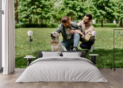 A gay couple with beards and casual attire spends a sunny day in a green park with their labrador retriever. Wall mural