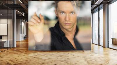 A handsome blonde man in stylish attire, viewed through a window reflection Wall mural