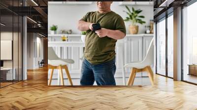 A man with inclusivity in casual attire stands in his home, looking at his phone. Wall mural