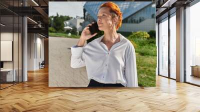 A woman in a white shirt talks on the phone while holding a blue folder on a college campus. Wall mural