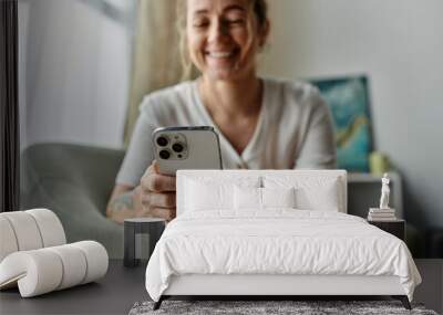 A woman with vitiligo smiles while looking at her phone on a cozy sofa. Wall mural