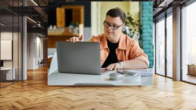 A young man with Down Syndrome is working on his laptop in a cafe, focused on his task. Wall mural