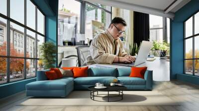 A young man with Down syndrome works on a laptop at a desk. Wall mural