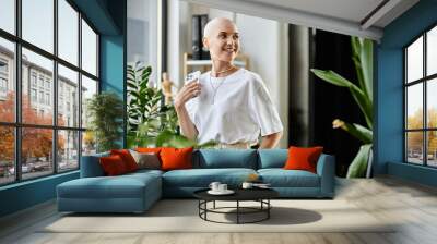 A young woman with a shaved head radiates confidence in stylish attire surrounded by plants. Wall mural