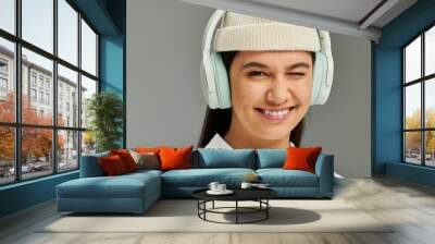 A young woman with an infectious smile expresses joy while wearing trendy headphones and a hat. Wall mural