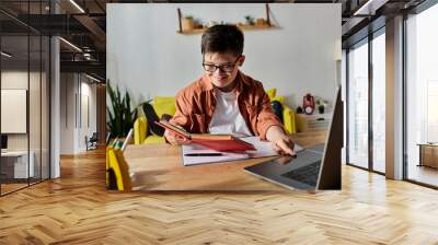 adorable boy with Down syndrome working on a laptop and reading a book at a table. Wall mural