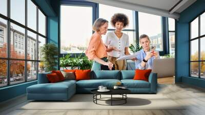 Diverse female professionals gather around a laptop for a productive work session. Wall mural