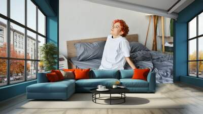 good looking extravagant person in white t shirt with red hair sitting on her bed, leisure time Wall mural