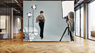 Middle-aged lesbian couple in a vibrant studio setting - one photographer with camera, the other posing as a model. Wall mural