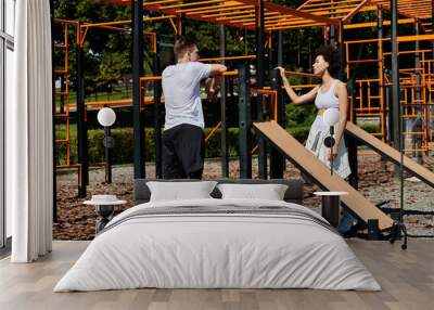 Two friends collaborate in an outdoor workout, exemplifying resilience and support in a vibrant environment, man with prosthetic leg Wall mural