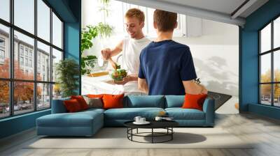 Two men create a delicious lunch together, sharing laughter in their stylish kitchen space. Wall mural