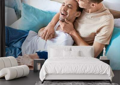 Two men in casual attire laying on a bed together. Wall mural