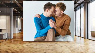 Two men in casual attire sitting on a white surface, showcasing a loving bond. Wall mural