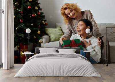 Two women exchange gifts in a cozy, festively decorated living room. Wall mural