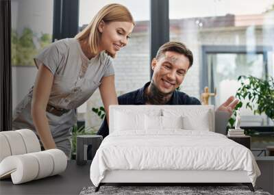 Two young professionals discuss ideas while working on a laptop in a modern office setting. Wall mural