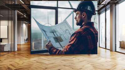 A construction worker reviewing blueprints in front of a window with a wind turbine in the background Wall mural