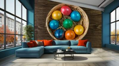 Colored Easter eggs in a basket on rustic wooden table. Wall mural