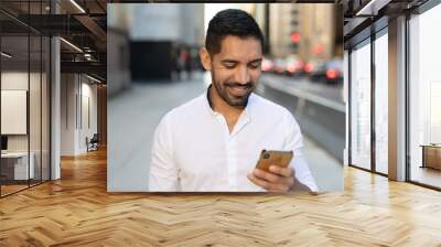 Young Latino Hispanic man in city walking texting cell phone Wall mural