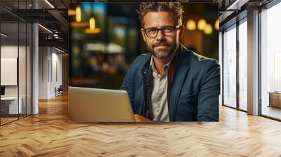 work life balance with remote work -middle aged man  wearing glasses and beard working on a laptop outside with bokeh of lights in a city in the background Wall mural