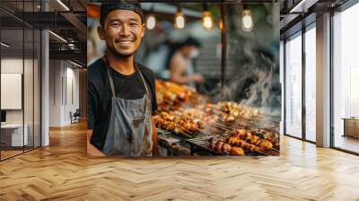 Man is smiling and standing next to a grill with food on it. He is wearing an apron and a hat Wall mural