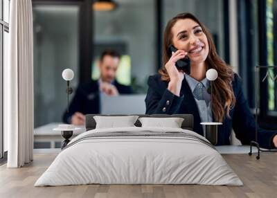 A happy businesswoman talking on a mobile phone while sitting at the office with a male colleague. Wall mural