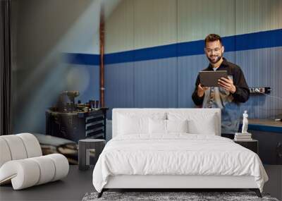 A smiling auto mechanic working at his garage, using a digital tablet. Wall mural