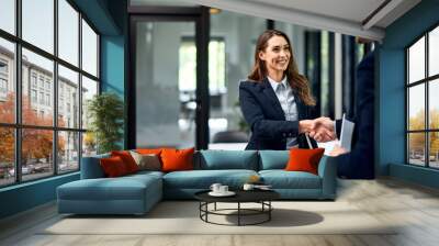 A smiling female employee handshake with a male boss at the office, elegantly dressed. Wall mural