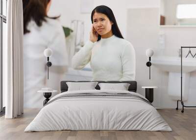 An adult Asian sick female has ear pain touching her painful head, sitting at the clinic. Wall mural