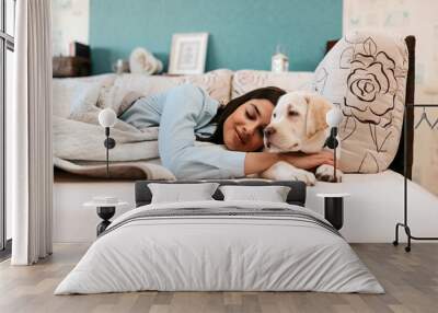 Attractive young girl with dog laying on a bed. Wall mural