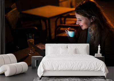 Blogger girl drinking coffee and working at night on a laptop, outdoors. High ISO image. Wall mural