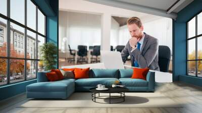 Businessman working on laptop in office, being concerned. Wall mural