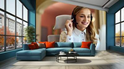 Close-up of a smiling businesswoman talking to a client over the microphone, using headphones. Wall mural