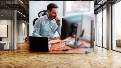 Concentrated businessman analyzing graphs in his office at computer. Wall mural