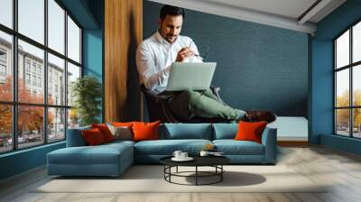 Elegant man using laptop while sitting in the armchair, portrait. Wall mural