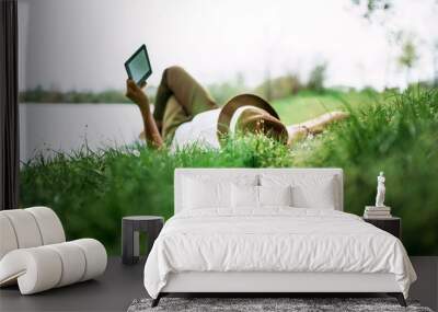 Enjoying e-book near the lake. Girl lying in the grass. Wall mural