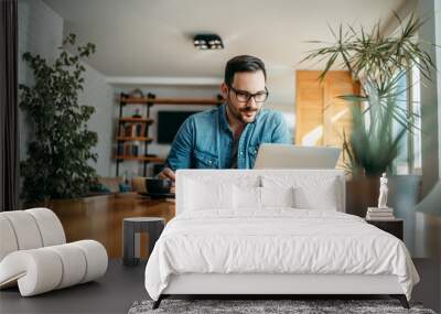 Handsome man taking notes and looking at laptop, at home office, portrait. Wall mural