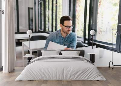 Handsome man working on laptop and holding documents. Wall mural