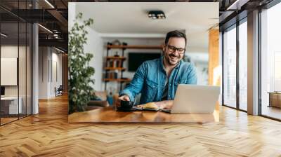 Happy entrepreneur at home office, looking at laptop and drinking cup of coffee, portrait. Wall mural