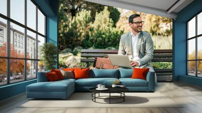 Happy young business man sitting on the bench with laptop. Wall mural