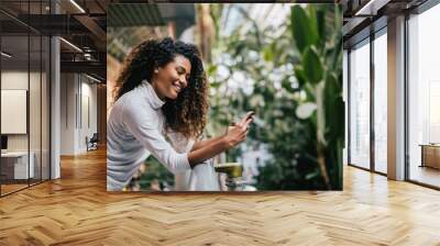 Indoor shot of dark skinned girl with cute smile using her phone. Wall mural