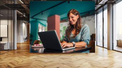 Low angle portrait of a cheerful woman using laptop in the cafe. Wall mural