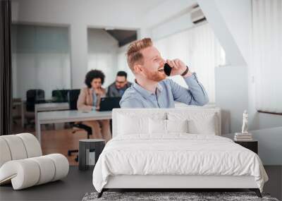 Millennial businessman talking on mobile phone in modern co working office. Wall mural