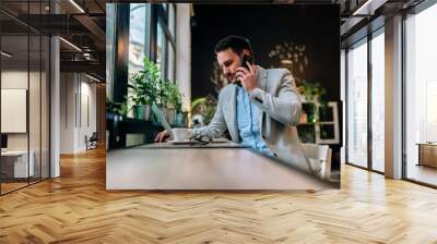 Modern businessman talking on a smartphone while working on laptop in the cafe. Wall mural