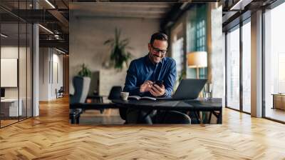 Photo of a smiling man using a mobile phone while being at the office. Wall mural