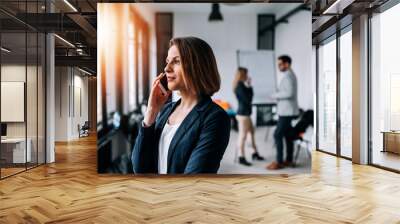 Portrait of a beautiful business woman talking on a phone in the office with collegues at the background. Wall mural