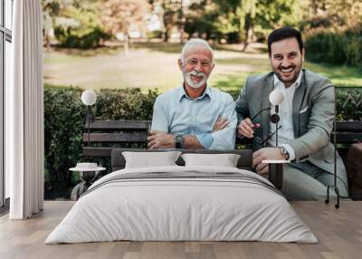 Portrait of a business family outdoors. Two men sitting in the park looking at camera. Wall mural