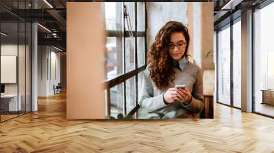 Portrait of a casual girl using a smart phone with a warm light near a window. Wall mural